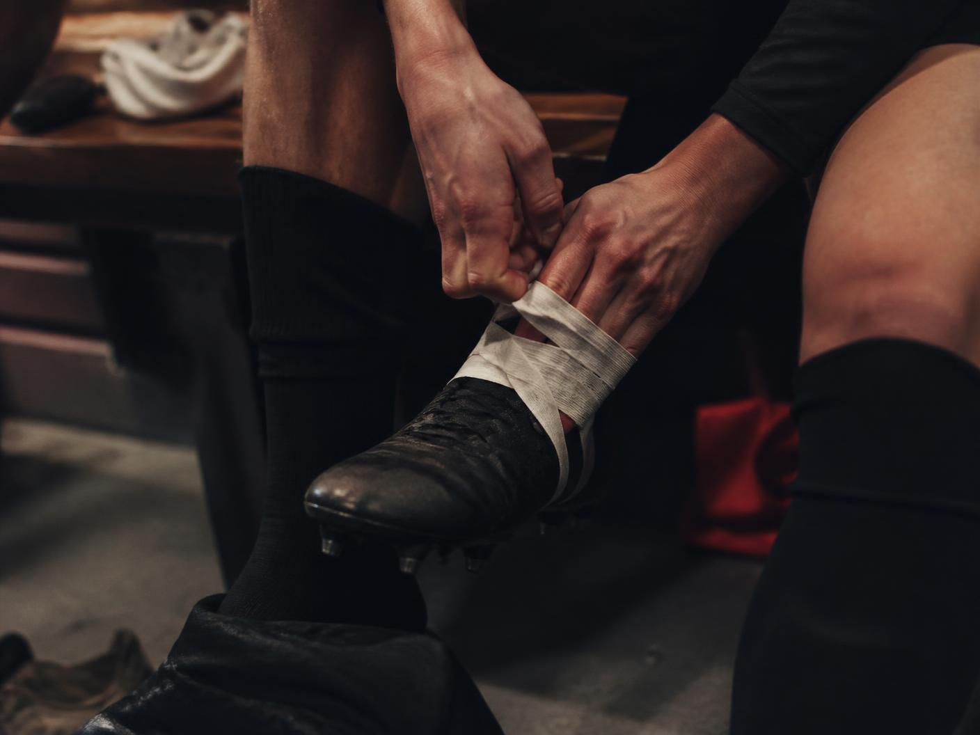 Footballer taping boots in a changing room before kick-off